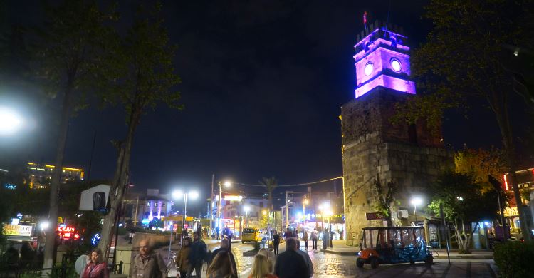 Der Uhrtrum Saat Kulesi ist in violetter Farbe beleuchtet und es gehen sehr viele Menschen der Straße entlang.