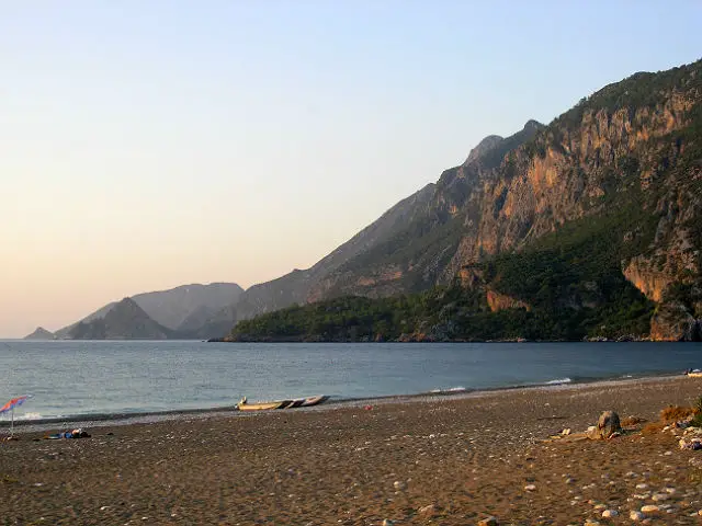 Olympos Beach am Abend bei Sonnenuntergang. Es sind keine Touristen mehr am Strand zu sehen. Der Blick geht auf das Meer und auf der rechten Seite gelegene Hügel mit Pinienwälder hinauf.