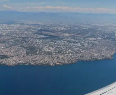 Blick auf den Flügel eines Flugzeuges und das darunterliegende Antalya mit den Landebahnen des Flughafen Antalya.