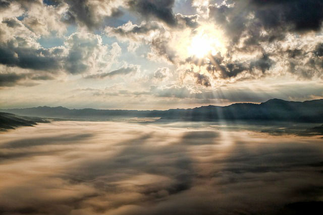 Blick auf eine dichte Wolkendecke von einem Flugzeug aus gesehen. Am Horizont ist die untergehende Sonne zu sehen. 