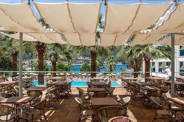 Restaurant in einem Clubhotel in der Türkei. Es ist mit weißen Tüchern überdacht. Der Blick geht Richtung der Poollandschaft. Im Hintergrund ist das Meer zu sehen.