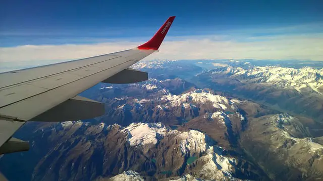 Flügel eines Flugzeges. Fotografiert aus dem Fenster in der Luft. Darunter sind die Alpen zu sehen.