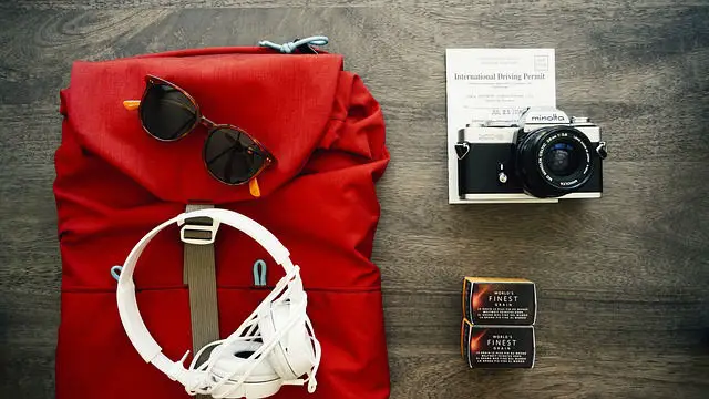 Roter Rucksack mit einer Sonnenbrille, Kopfhörern und einer Fotokamera auf einem Tisch liegend