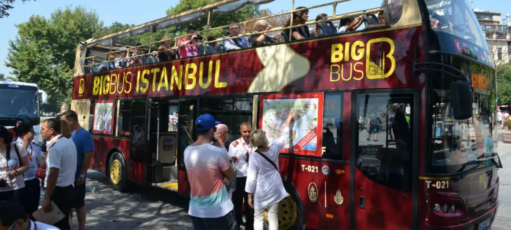 Big Bus für eine Stadtrundfahrt durch Istanbul. Ein roter Doppeldeckerbus der oben offen ist und eine gelbe Aufschrift mit dem Namen des Busunternehmens trägt. Es steigen gerade Fahrgäste ein und aus.