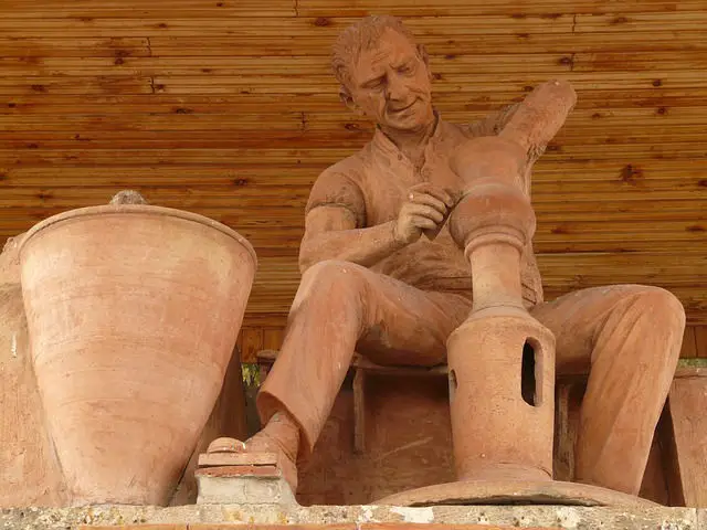 Eine aus Ton gebrannte Statue eines Töpfers. Er dreht gerade einen neuen Krug. Daneben steht ein großer Tonkrug.