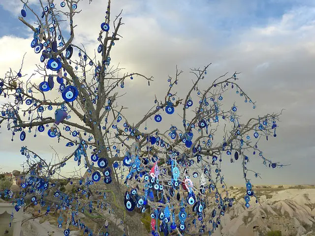 Dutzende Türkische Augen hängen an einem Baum. Dahinter ist die Landschaft in Kappadokien zu sehen. 