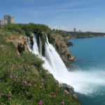 Auf der oberen Seite der Klippen sind ein paar Blumen zu sehen. Das Wasser des Düden Wasserfalls.