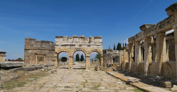 Das aus drei Torbögen bestehende Westtor von Hierapolis. Es ist noch gut erhalten. Auf der linken Seite sind die Reste eines Turms zu sehen. Rechts sind die Ruinen der Latrinen. 