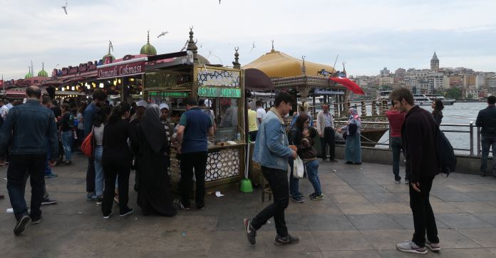 Balik Ekmek Boot und davor ist ein Verkaufsstand mit sehr vielen Menschen zu sehen. 