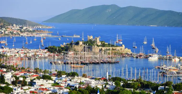 Blick von einem Hügel auf den Hafen und die Burg von Bodrum. Es sind viele Segelschiffe zu sehen. Dahinter sind Inseln zu sehen. 