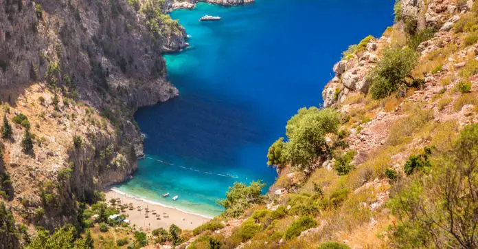 Blick von den 300 Meter hohen Wänden des Steilen Butterfly Valley auf den am Ende gelegene schmalen Sandstrand, das türlisblaue Meereswasser in der Bucht davor und ein kleines Boot.