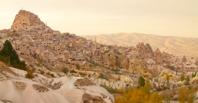 Blick auf die Festung Uchisar im Morgenrot. Dahinter sind Dünen zu sehen und rötlich gefärbte Wolken