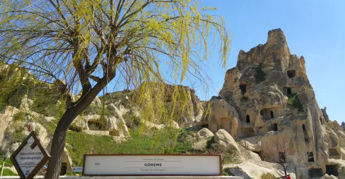 Eingangsschild zum Freilichtmurseum Göreme mit einem Baum davor und einem in Stein gehauenen Bauwerk