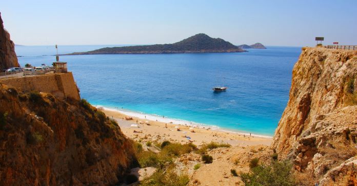 Foto von der Straße oberhalb der Steilküste auf den darunterliegenden Sandtrand Kaputas Beach. Im Hintergrund ist das türkisblaue Meer und kleine Inseln zu sehen.