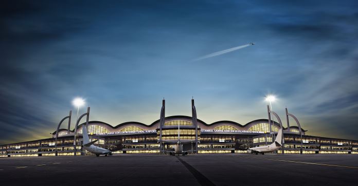 Flughafen Istanbul Sabiha Gökcen in der Nacht von der Parkbuchten der Flugzeuge aus augenommen. Mit einem fliegenden Flugzeug über dem Terminalgebäude. 