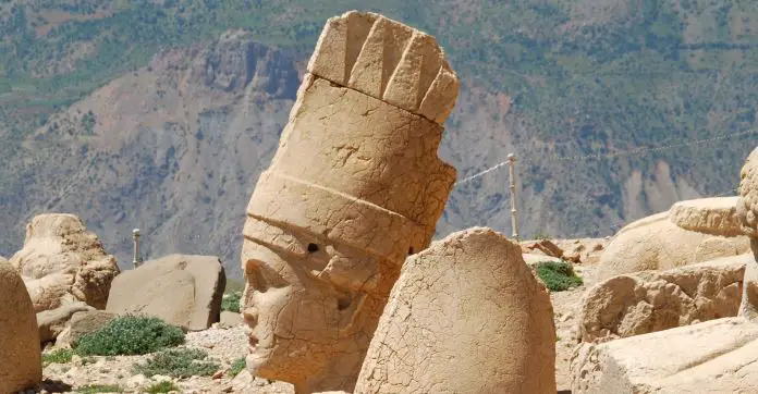 Mehrere Meter hoher Kopf einer Götterstatue am Nemrut Dagi. Mit Blick auf einen danebenliegenden Berghang.
