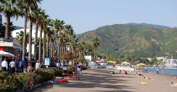 Sandstrand in Marmaris, mit Liegestühlen, Palmen, Meer und Blick auf die Berge im Hintergrund