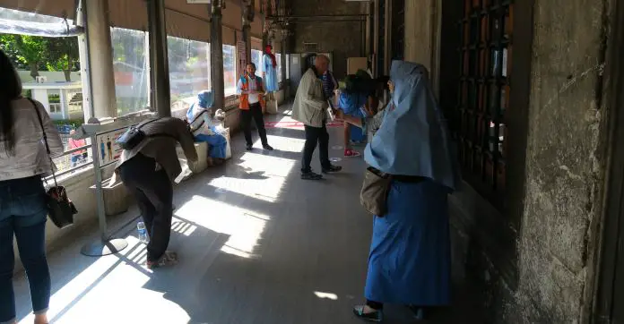 Besuchereinang auf der rechten Seite der Moschee mit Sitzbänken um Schuhe auszuziehen und den blauen Röcken und Kopftüchern, die für Frauen verteilt werden. 