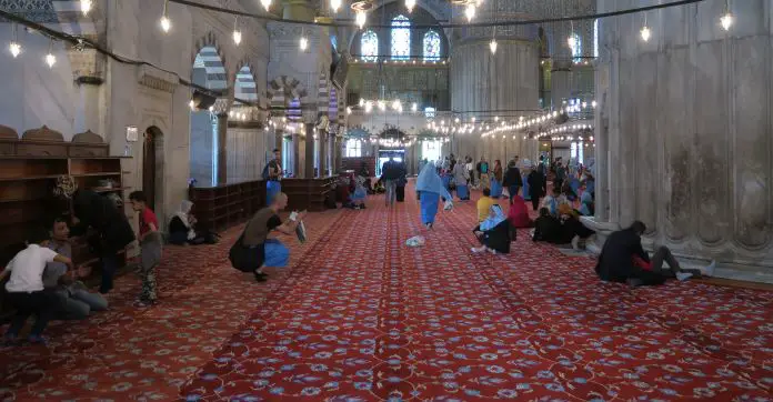 Die Schuhregale am Eingang der Blauen Moschee, im hinteren Bereich der Moschee. Es sind viele Touristen mit den blauen Koptüchern und Röcken zu sehen. Touristen machen Fotos.