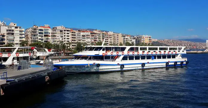 Eine weiße Fähre mit Passagieren und türkischen Flaggen an Deck legt am Hafen an.