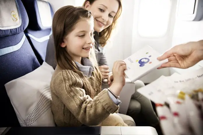 Foto vom Gang eines Flugzeuges mit Blick auf die Sitzreihe. Darin sitzt ein Mächden und ihre Mutter. 