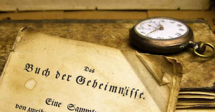 Eine Taschenuhr liegt neben einem vergilbten Dokument mit der Aufschrifft "Geheimnisse". 