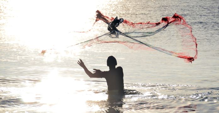 Ein Fischer steht im Meer. Er wirft gerade sein Netz aus. 