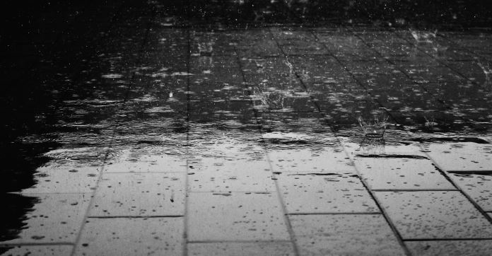 Scwarz-Weiß Aufnahme von Regentropfen, die auf eine Straße fallen. Das Bild wirkt melancholisch.