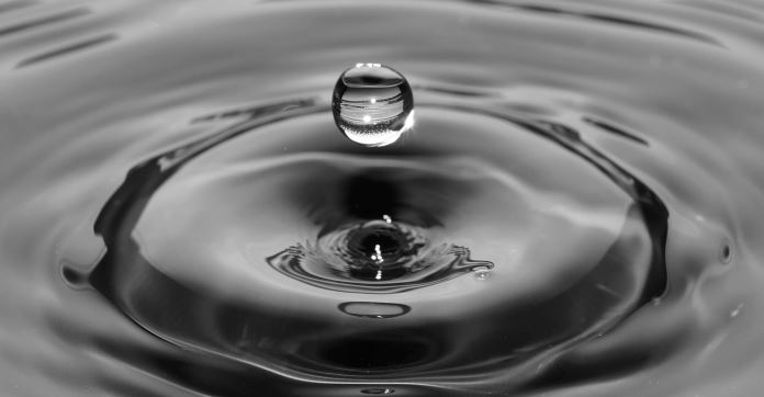Ein Wassertropfen ist ins Wasser gefallen und springt wieder ein wenig hoch.