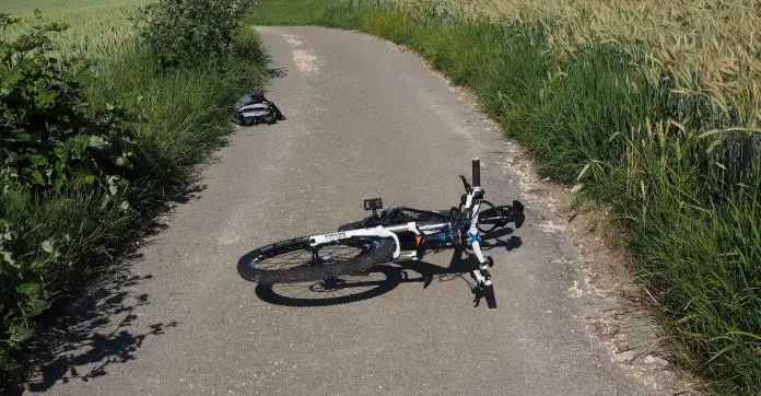 Ein Rad ist auf einem schmalen Feldweg umgefallen. Es liegt Mitten am Weg. Daneben sind Felder. 