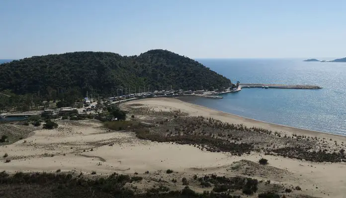 Der Sandstrand von Andriake mit dem kleinen Hafen und einer bewaldeten Halbinsel im Hintergrund. 