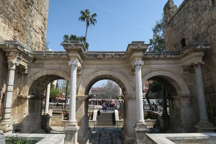 Das aus Marmor gebaute Hadrianstor besteht aus drei Torbögen und steht zwischen zwei hohen sandsteinfarbenen Türmen an den Stadtmauern der Altstadt von Antalya. 