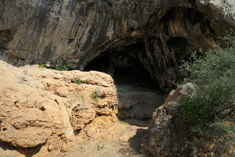 Der mehrere Meter hohe Haupteingang der Karain Höhle. Die Steine sind im unteren Bereich Sandfarben und im oberen Bereich grau. 