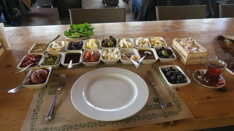 Die kleinen Schalen mit den verschiedenen Gerichten zum Früstück, wie es in der Türkei üblich sind. Sie sind in kleinen, weißen Schalen neben einem Teller auf dem Tisch angerichtet. 