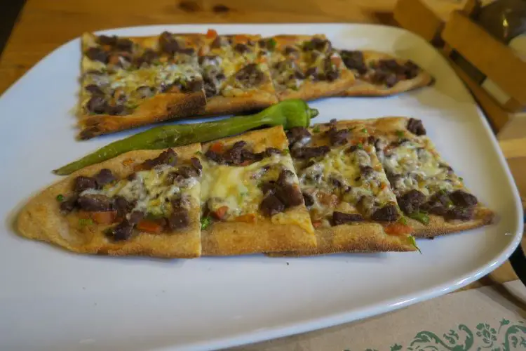 Die Nahaufnahme eines weißen Tellers mit zwei Stück Pide auf einem Holztisch. 