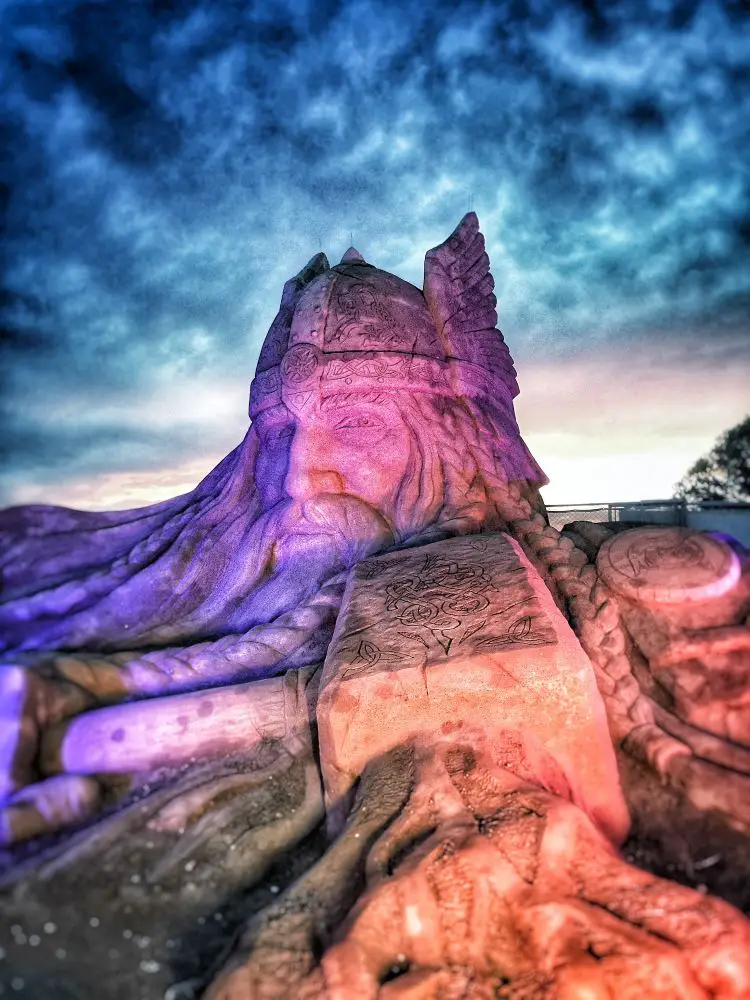 Eine in violetter Farbe beleuchtete Sandskulptur des Kopfes von Thor und seinem Hammer Mjölnir. Die Statue ist in etwa 5 Meter hoch. 