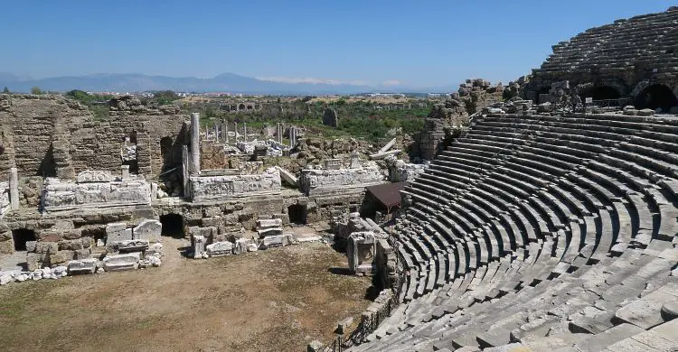 Der Ausblick vom obersten Sitzrang des Theaters von Side auf die hinter dem Bunenhaus liegenden Ruinen und die Berge des Taurus im Hintergrund.