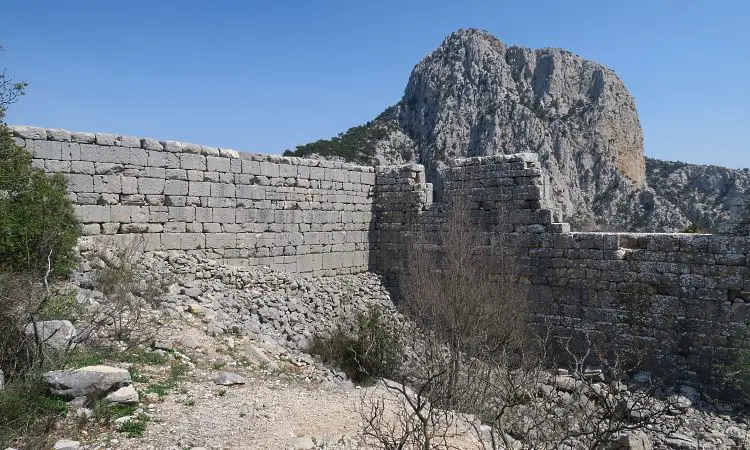 Die umfassenden Mauern des Odeon von Termessos mit Nadelbäumen auf der rechten Seite und einem Berg im Hintergrund. 