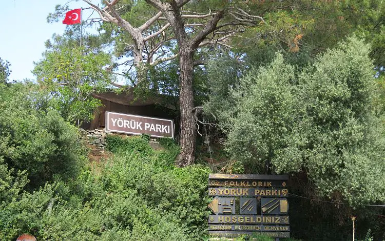 Das braune Willkomensschild mit der weißen Aufschrift: Yörük Park". Es ist von Sträuchern und Laubbäumen umrahmt.