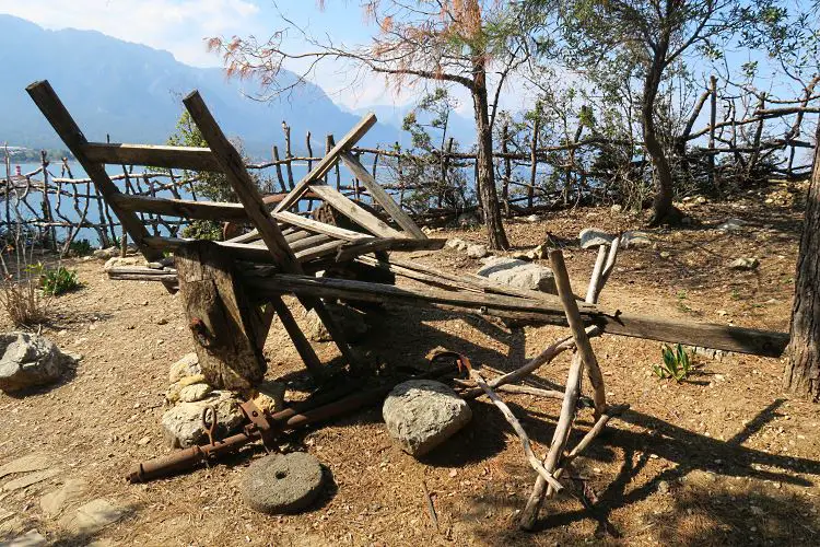 Ein Holzwagen steht im Yörük Nomaden Park. Dahinter ist ein Holzzaun und das Mittelmeer zu sehen. 