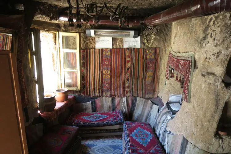 Es sind Sitzbänke, Teppiche und ein Fenster in einem Höhlenhaus in Kappadokien zu sehen.