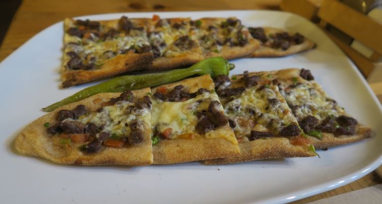 Ein Teller mit dem typisch türkischen Gericht Pide. Sie sind oval geformt und erinnern an Pizza. Sie sind mit Hackfleich, Zwiebeln und Käse belegt. 