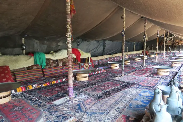 Ein großes Zelt mit Sitzgelegenheiten am Boden im Yörük Nomaden Park in Kemer. Das Zeltdch ist grau-braun und die Sitze sind rot. 