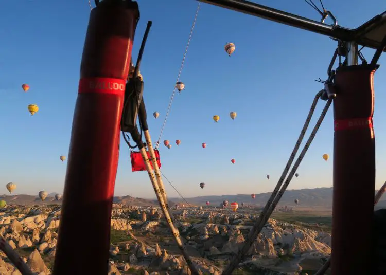 Blick aus dem Korb eines Heißluftballons auf Kappadokien und den Himmel voller anderer Ballone. 