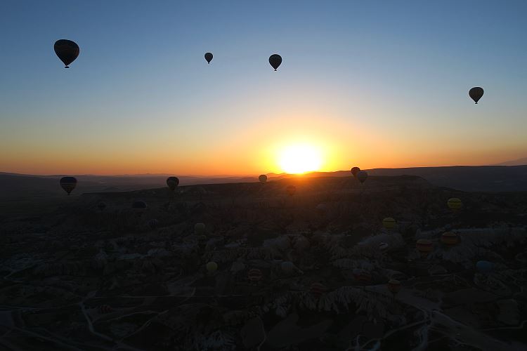 Die Sonne geht über Kappadokien auf. Das Bild zeigt einige Heißluftballone vor der Sonne. Es wurde aus einem Heißluftballon aufgenommen.