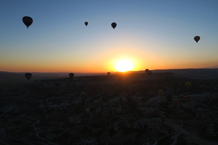 Die Sonne geht über Kappadokien auf. Das Bild zeigt einige Heißluftballone vor der Sonne. Es wurde aus einem Heißluftballon aufgenommen. 