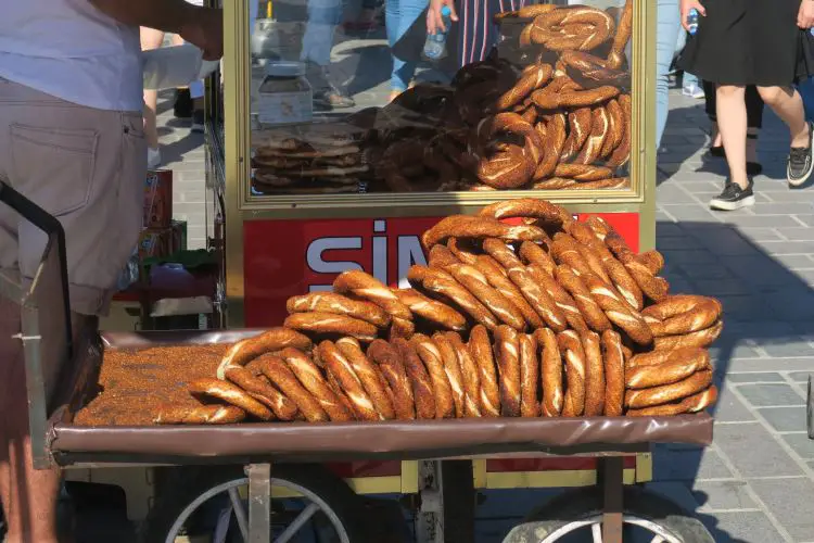 Ein Stand mit Simit steht auf einem Platz mit vielen Menschen. 