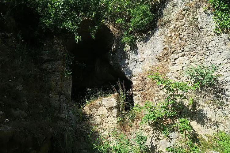 Der Eingang in eine Höhle ist mit einem Steinbogen zusätzlich abgesichert. Er liegt an einem bewachsenen Hügel. 