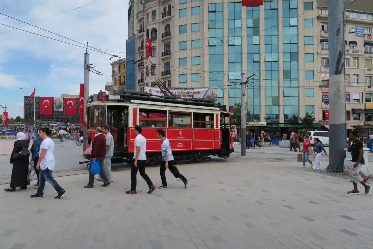 Eine rote Straßenbahn fährt in die Istiklal Caddesi, vom Taksim Platz. Vorbei an Läden die Hamburger verkaufen.