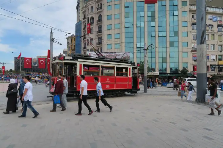 Eine rote Straßenbahn fährt in die Istiklal Caddesi, vom Taksim Platz. Vorbei an Läden die Hamburger verkaufen. 